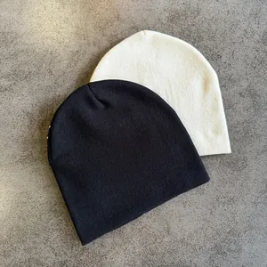 Flat lay detail of black and cream knitted beanies on a grey textured surface