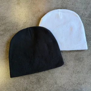 Flat lay detail of minimalist black and white knitted beanies on textured background