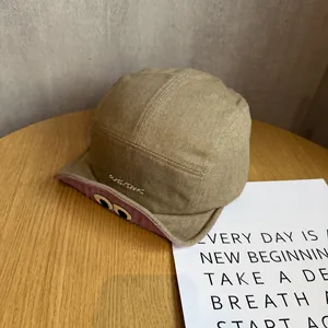Detail of khaki camp cap featuring cartoon eye embroidery under pink short brim