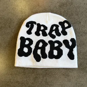 Detailed view of white knit beanie with TRAP BABY jacquard lettering in street style