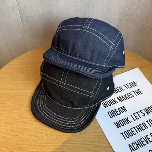 Detail of navy and black denim camping hats featuring contrast white stitching on wood
