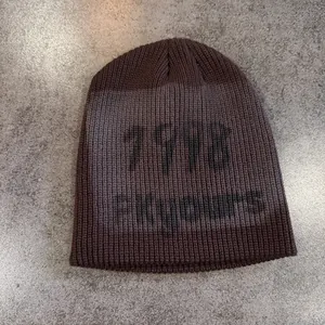 Close-up of dark brown knit beanie featuring black 1918 ENCORE text on grey stone surface