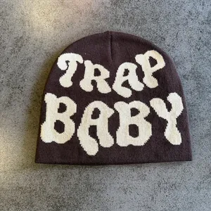 Close-up of knit beanie showing white TRAP BABY jacquard letters on dark brown wool fabric