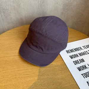 Detail shot of a purple 5-panel canvas cap showing fabric texture on a wooden table