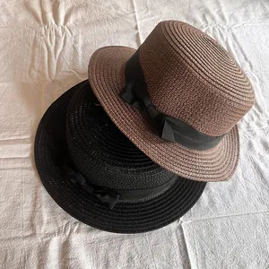 Flache Strohhüte in Braun und Schwarz mit Seidenschleife auf weißem Hintergrund