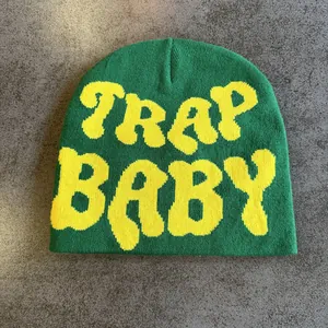 Detail of green knitted beanie featuring bold yellow TRAP BABY jacquard lettering