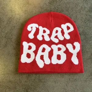 Close-up of red knit beanie featuring white TRAP BABY jacquard lettering texture