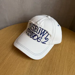 Close-up of blue letter embroidery with distressed frayed edges on a white cotton baseball cap