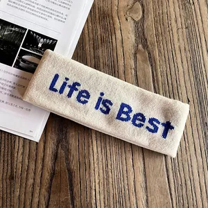 Détail d'un bandeau en tricot beige avec broderie Life is Best bleue sur bois