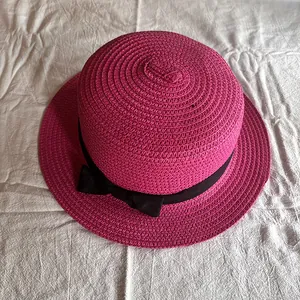 Draufsicht auf einen rosa Strohhut mit schwarzer Schleife auf weißem Stoffuntergrund
