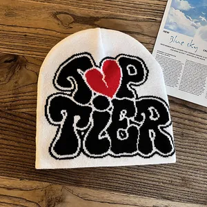 Close-up of white knit beanie featuring Top Tier text and red broken heart jacquard pattern