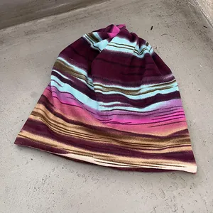 Flat lay detail of a striped knit slouchy beanie in purple and blue on a gray texture