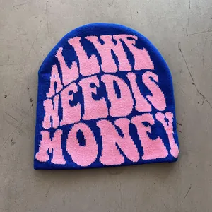 Detail of royal blue knitted beanie with pink jacquard slogan text on gray surface