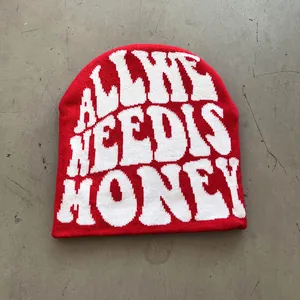 Detailed close-up of red knit beanie with white jacquard lettering on cement ground