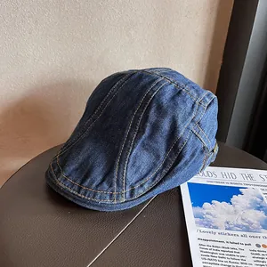 Detail of dark blue denim newsboy cap with contrasting yellow stitching and metal buckle