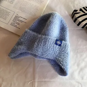 Detail of light blue fuzzy knit hat featuring a snowflake patch on a white background