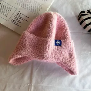 Detail of pink faux mohair knit trapper hat featuring a blue snowflake patch on soft fabric