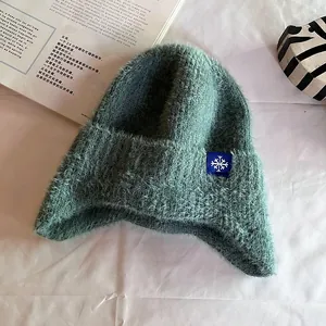 Detail of grey-green plush knit hat showing soft fuzzy texture and snowflake patch