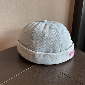 Dettaglio del berretto docker in denim azzurro con ricamo rosa Music sul lato