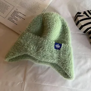 Close-up of light green knit earflap hat showing soft faux mink fur and snowflake patch