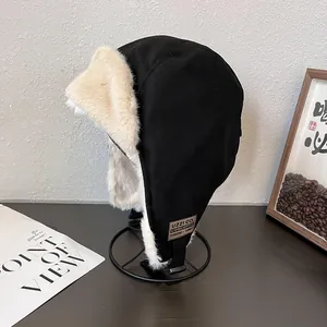 Detail of black trapper hat with thick beige faux fur lining and leather logo patch
