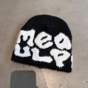 Close-up of soft black plush beanie with white Mea ulp knit lettering on concrete background