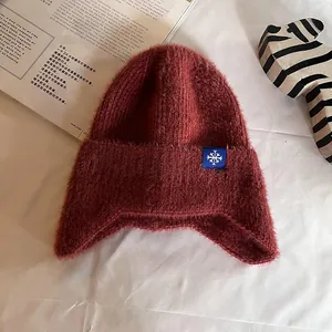 Close-up of deep red thick knit earflap hat with soft fuzzy texture and snowflake label