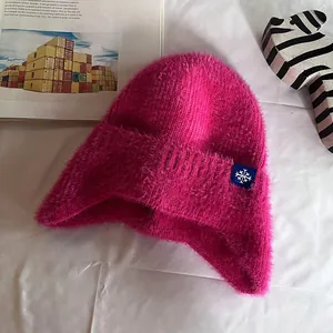 Close-up of fluffy pink knit earflap hat with snowflake patch on white fabric background