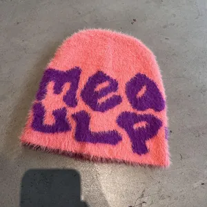 Close-up of pink fuzzy knit beanie with purple jacquard letters and soft texture