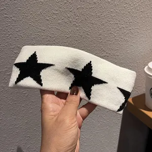 Close-up of a white knitted headband featuring black star patterns and soft woven texture