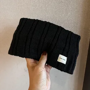 Detail of black ribbed knit headband showing thick texture and a white logo label