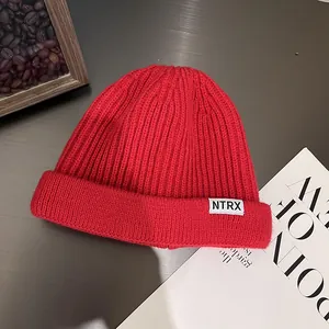Detail of red ribbed knit beanie with small white NTRX label on a textured desk