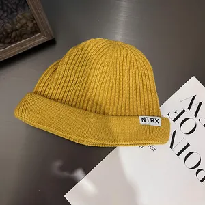 Detail of a ginger yellow ribbed knit beanie with a white NTRX letter patch label
