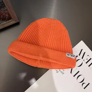 Detail view of the chunky ribbed knit texture and lettered label on this orange beanie