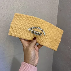 Detail of yellow chunky knit headband featuring black woven label with white text