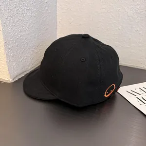 Detail of black short brim baseball cap showing orange smile embroidery and twill texture