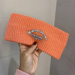 Detail of a bright coral orange knitted headband featuring a modern couture woven label