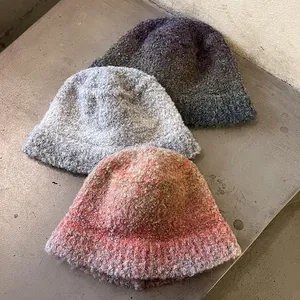 Three mixed color bouclé knit bucket hats in grey, purple and coral on concrete background