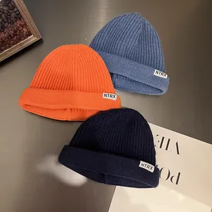 Three colorful knitted beanies in orange and blue with NTRX patches on metal desk
