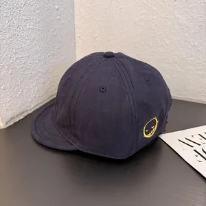 Detailed view of yellow smiley face embroidery on a navy blue short brim baseball cap