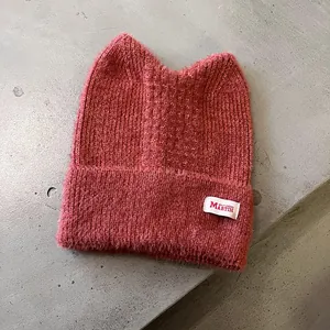 Detail der dunkelrosa Strickmütze mit süßen Katzenohren und gewebtem Textiletikett