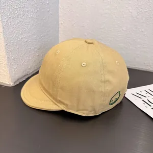 Detailed close-up of khaki short brim baseball cap with green embroidered smile face