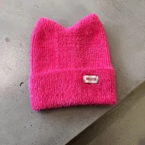 Details einer rosaroten Strickmütze mit Katzenohren aus flauschigem Webpelz und Etikett