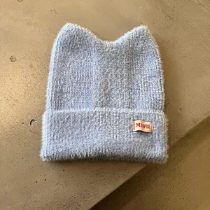 Detail der hellblauen flauschigen Strickmütze mit Katzenohren und Leder-Label-Dekor