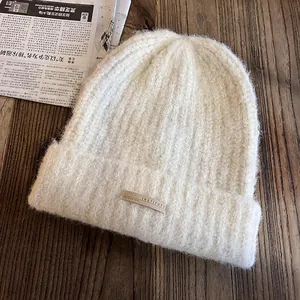 Détail du bonnet en maille crème avec texture pelucheuse et étiquette INSTITUTE