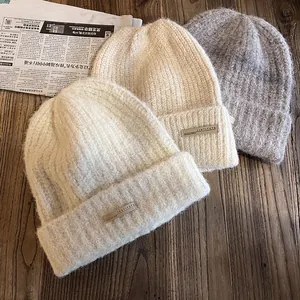 Trois bonnets en maille chaude en crème, beige et gris avec une texture douce et étiquette