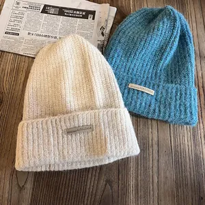 Bonnets d'hiver en grosse maille de couleur crème et bleu sur fond en bois
