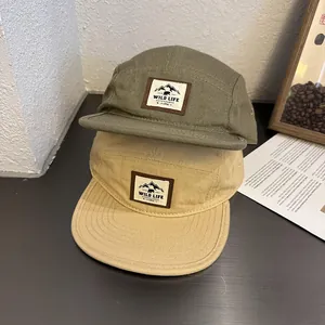 Close-up of olive and khaki five-panel camper caps with Wild Life mountain labels