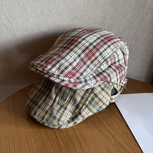 Classic checkered newsboy caps in red and khaki green patterns on a wooden table