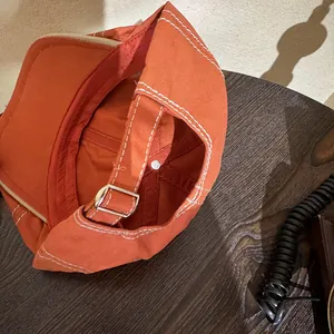 Detail of vintage orange newsboy hat showing white contrast stitching and adjustable metal buckle